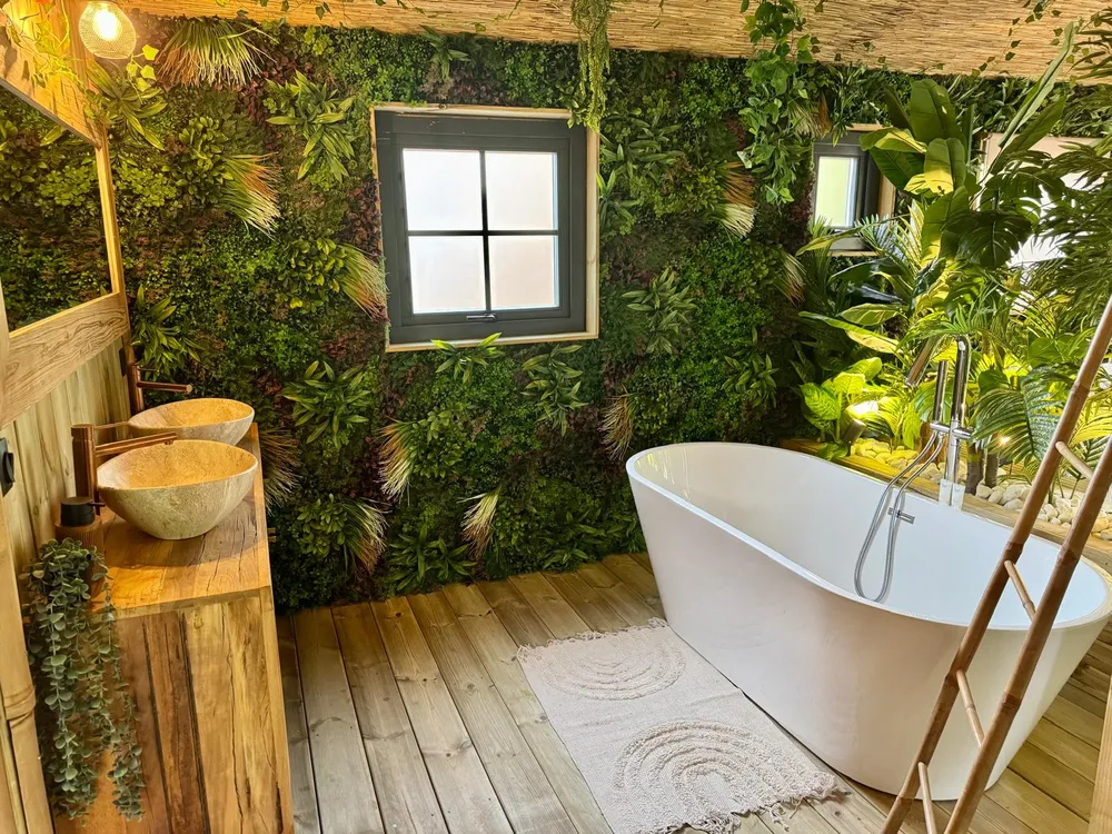 Baignoire blanche au centre de la pièce de vie du Jungle Lodge, sous un plafond en roseaux et entourée de végétation tropicale